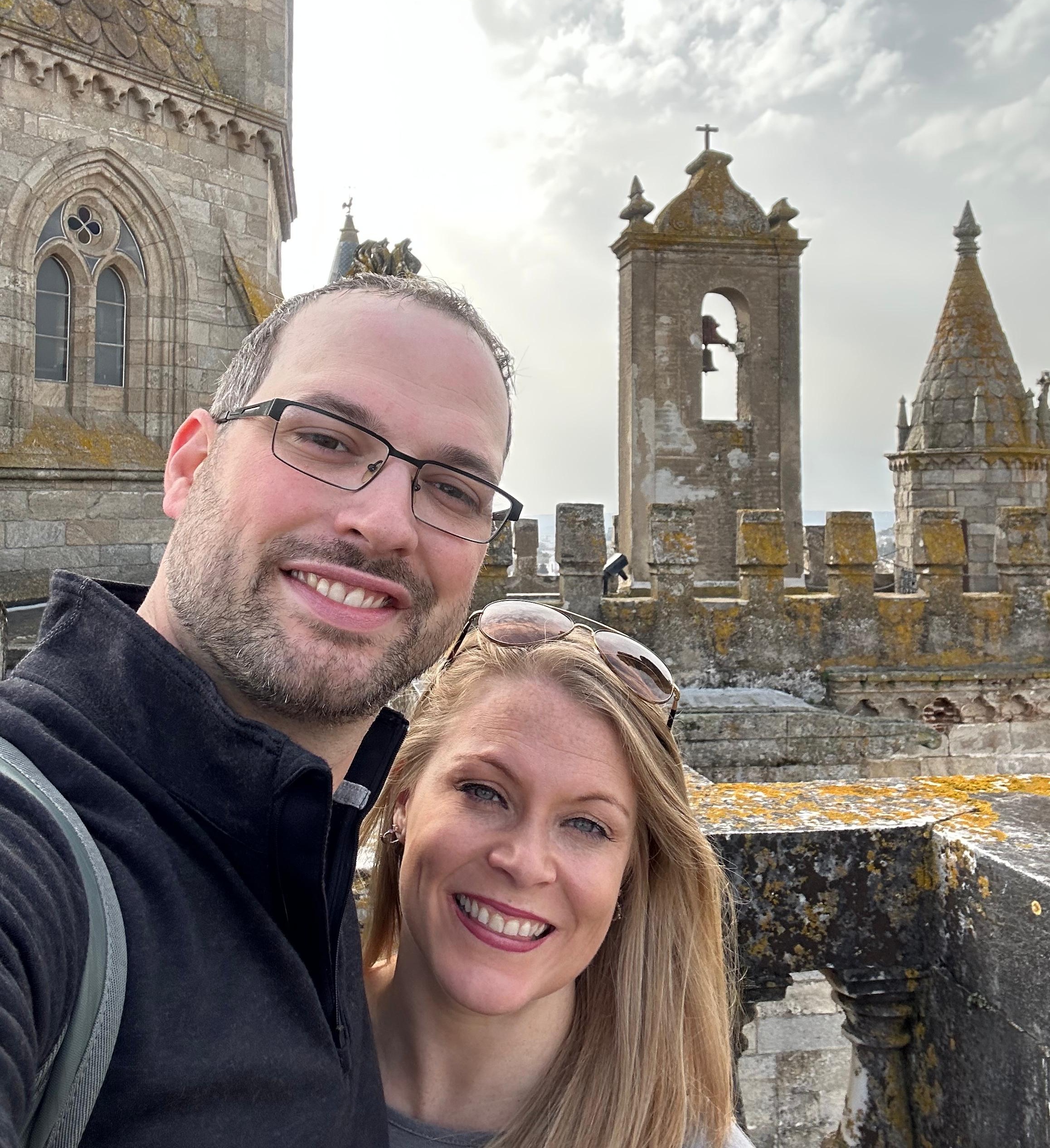 A man and a woman smiling, with old stone buildings in the background